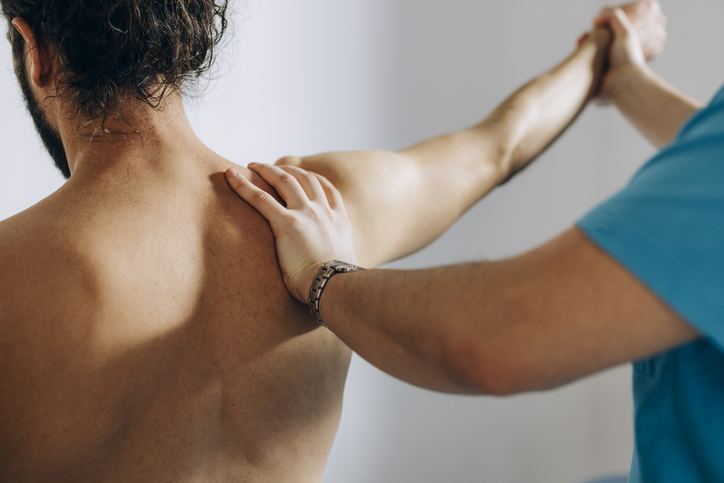 Physical Therapy: Chiropractor Doing Shoulder Adjustment While Patient is Sitting on the Bed Handtherapie